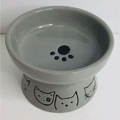 a ceramic bowl with cats painted on the side and black dots in the bottom, sitting on a white surface