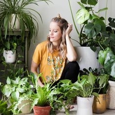 a woman sitting on the floor surrounded by potted plants