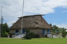 a thatched roof house with flags on the front lawn and stairs leading up to it