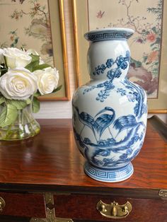 a blue and white vase sitting on top of a wooden table next to two flowers