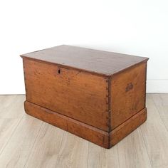 an old wooden box sitting on top of a hard wood floor next to a white wall