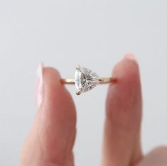 a woman's hand holding an engagement ring with a heart shaped diamond on it