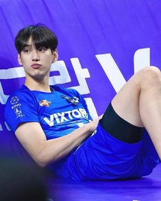 a young man sitting on the ground with his legs crossed in front of him, wearing a blue shirt and black shorts