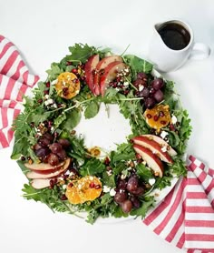 a wreath made out of apples, grapes and other fruits on a plate with a cup of coffee