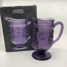 a purple glass pitcher next to a boxed box for the modern village coffee cup set