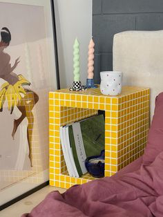 a bed with a pink comforter next to a yellow and white cube end table