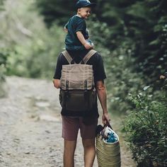 a man carrying a child on his back while walking down a path in the woods