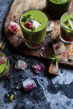 three glasses filled with green smoothie on top of a cutting board next to ice cubes