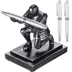 a statue with a pen on top of it next to some writing implements and pens