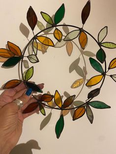 a hand is holding a piece of stained glass in the shape of a circle with leaves on it