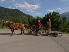 two people are riding in a horse drawn carriage on the road with mountains in the background