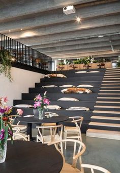 tables and chairs with flowers in vases on them at the bottom of some stairs