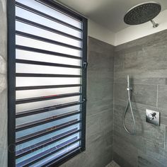 a bathroom with a shower head, window and tiled walls in grey tones on the wall