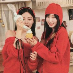 two young women in red sweaters standing next to each other and eating donuts