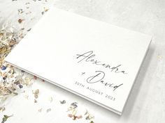 a wedding guest book with confetti scattered around it on a white tablecloth