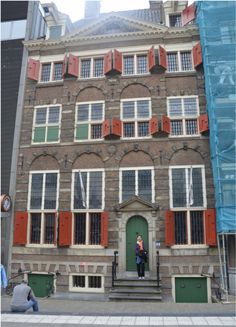 a person standing in front of a building with red shutters on the doors and windows