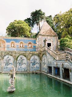 a fountain in front of a building with blue and white tiles on the walls, surrounded by trees