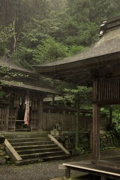 a wooden building in the middle of a forest with stairs leading up to it's roof