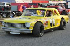 a yellow race car driving down a street with other cars in the backgroud