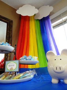 a table topped with a piggy bank next to a rainbow colored curtain and cake