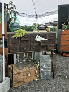 an old dresser with many drawers and plants on it's top, sitting under a tent