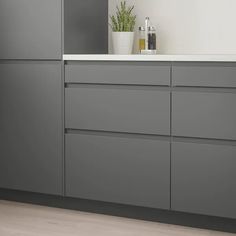 a kitchen with gray cabinets and white counter tops, along with a plant in the corner