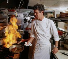 a man cooking food on top of a stove in a kitchen with flames coming out of it