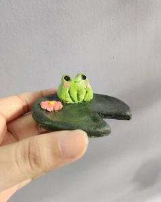 a hand holding a tiny frog sitting on top of a piece of green leafy material