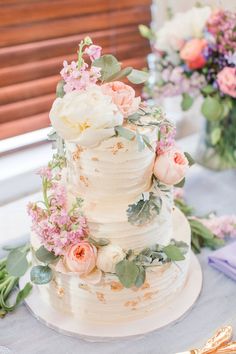 Spring wedding cake at reception. White 3 tiered buttercream with soft pastel colored flowers on the frosting. White Wedding Cake Pink Flowers, Bridgerton Pastel Wedding Theme, Aesthetic Wedding Cake Korean, Spring Pastel Wedding Cake, Spring Themed Wedding Cake, Peonies Wedding Cake, Pastel And Greenery Wedding, Pastel Wedding Flowers Table, Pastel Garden Wedding Theme