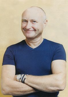 an older man with his arms crossed and wearing a blue t - shirt smiles at the camera