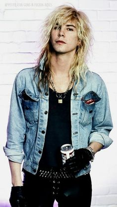 a man with long hair wearing black leather pants and a denim jacket holding a can of soda