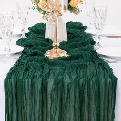 a table topped with a vase filled with yellow flowers and green ruffled cloth draped over it