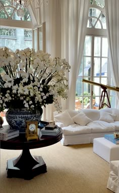 a living room filled with white furniture and lots of flowers in a vase on top of a table