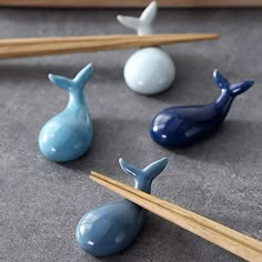 three small whale figurines sitting next to chopsticks on a gray surface