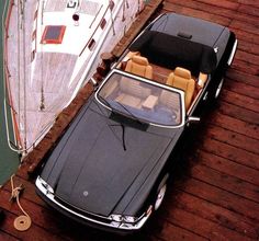 two cars parked next to each other on a wooden dock with a boat in the background