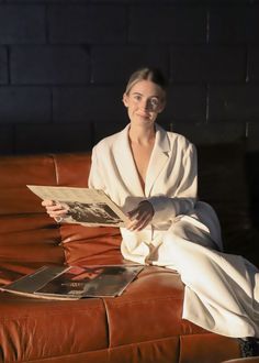 a woman sitting on top of a brown leather couch holding a magazine in her hands