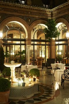 an indoor dining area with tables, chairs and potted plants in the center is lit up at night