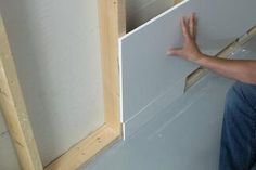 a man kneeling on the floor next to a white wall and holding his hand up