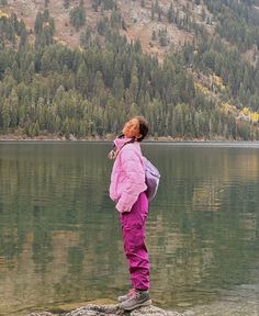 a woman standing on top of a rock next to a lake