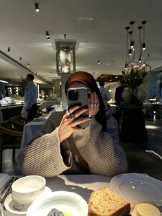 a woman taking a selfie with her phone at a table full of food and drinks