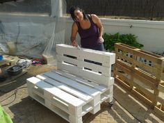 a woman standing next to a white bench made out of pallets