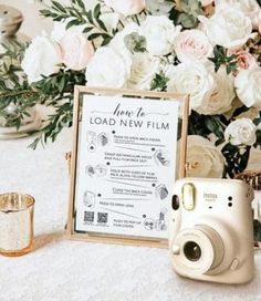 a white table topped with flowers and a camera next to a sign that says load new film