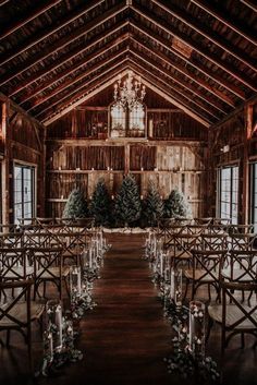 an indoor wedding venue set up with clear chairs and greenery on the aisle, surrounded by candles