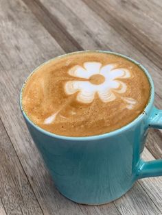 there is a cup of coffee with a flower on the foam in it, sitting on a wooden table