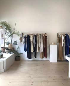 a room with clothes hanging on the wall and two tables in front of it,