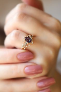 a woman's hand holding a gold ring with an oval shaped purple stone on it