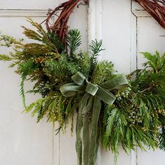 a wreath hanging on the side of a door with greenery and pine cones around it