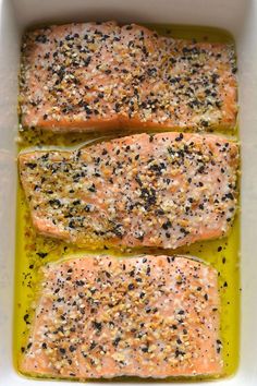 three salmon fillets in a white casserole dish with mustard and seasoning