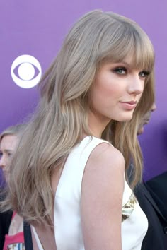 Taylor Swift Wavy Ash Blonde Straight Bangs Hairstyle | Steal Her Style Dark Blonde Hair Taylor Swift, Ashy Sandy Blonde Hair, Muted Ash Blonde Hair, Blonde Hair For Cool Toned Skin, Taylor Swift Hair Color 2023, Blonde Hair Taylor Swift, Sandy Ash Blonde Hair, Toning Hair Before And After, Taupe Blonde Hair