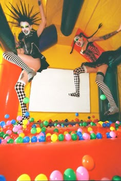 two women dressed as clowns sitting on top of an inflatable ball pit